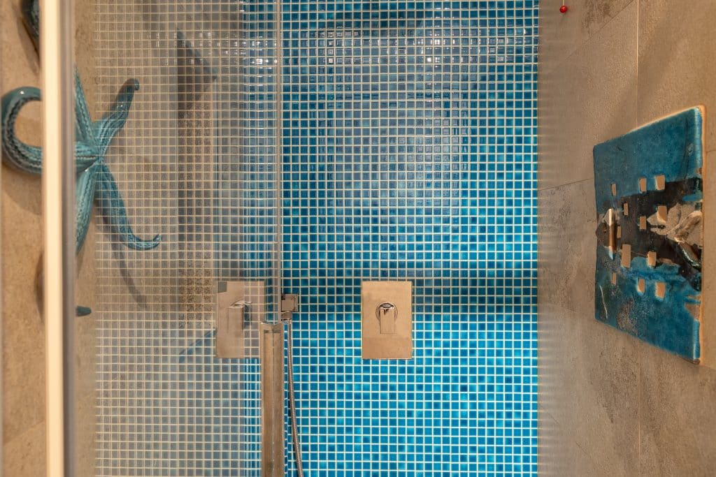 Modern bathroom with blue mosaic tiles, handcrafted ceramic decor and Mediterranean design details in an Alghero apartment, Sardinia. Bagno moderno con piastrelle a mosaico blu, decorazioni in ceramica artigianale e dettagli di design mediterraneo in appartamento ad Alghero, Sardegna.