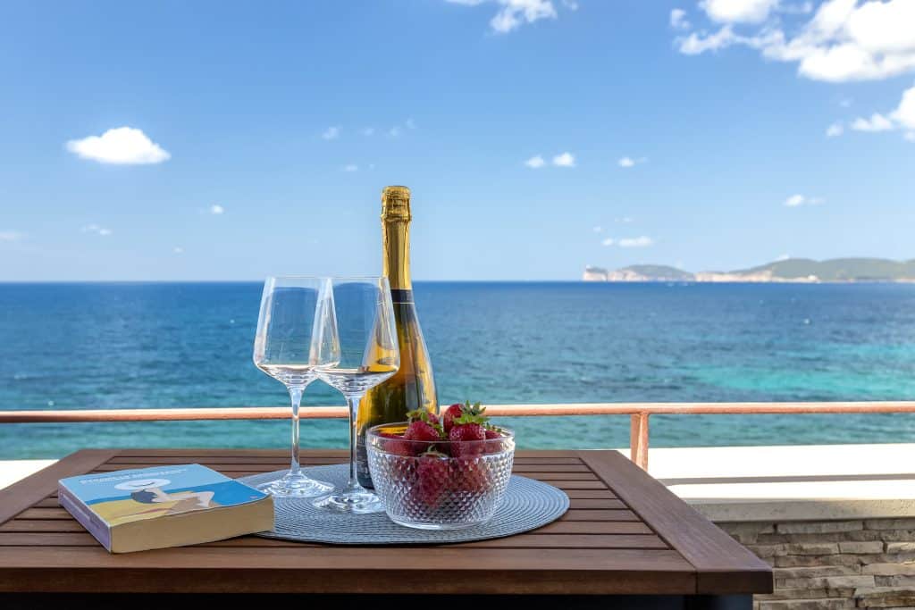 Sea view terrace with Akenta sparkling wine and fresh strawberries from Alghero market, overlooking Capo Caccia, Sardinia. Terrazza vista mare con vino spumante Akenta e fragole fresche dal mercato di Alghero, con vista su Capo Caccia, Sardegna.